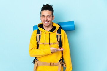 Young mountaineer man with a big backpack over isolated blue background extending hands to the side...