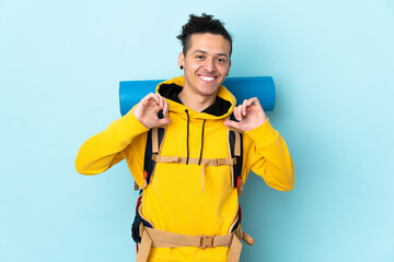 Young mountaineer man with a big backpack over isolated blue background proud and self-satisfied