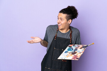 Young artist man holding a palette over isolated purple background with surprise facial expression
