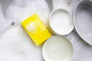 Dirty dishes with cleaning sponge in foam of dishwashing liquid. Washing dishes concept