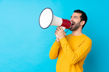 Young caucasian man over isolated blue background shouting through a megaphone