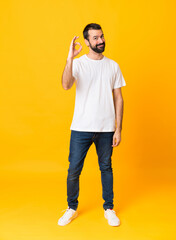 Full-length shot of man with beard over isolated yellow background showing ok sign with fingers