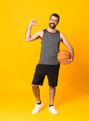 Full-length shot of man over isolated yellow background playing basketball and proud of himself