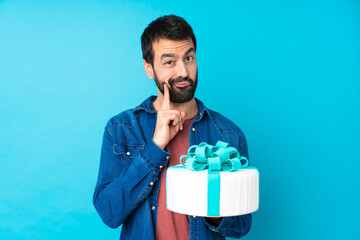 Young handsome man with a big cake over isolated blue background and looking front