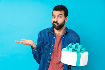 Young handsome man with a big cake over isolated blue background unhappy for not understand...