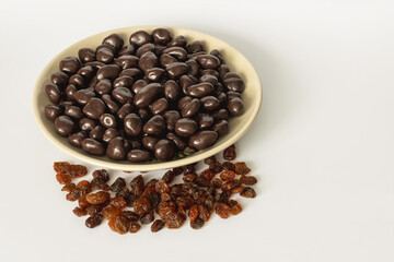 Dried raisins with dark chocolate in a bowl on a light gray background