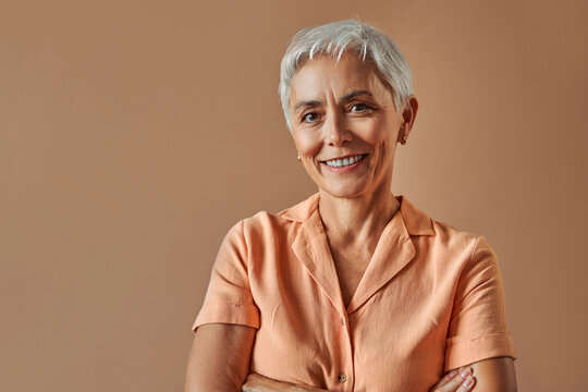 Woman's beauty and maturity. Portrait of a beautiful gray-haired woman with a short hairstyle on a beige background.