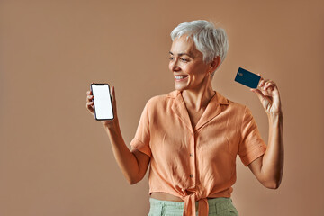 A sincere mature beautiful gray-haired woman in a pastel orange shirt and green pants holds a...