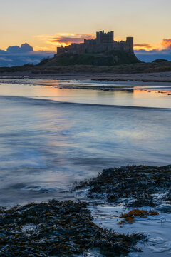 Beautiful landscape image of Northumberland beach in Northern England during Winter dawn with deep orange sky