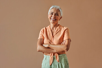 Woman's beauty and maturity. Portrait of a beautiful gray-haired woman with a short hairstyle, stylishly dressed in a pastel orange shirt and green pants.