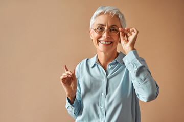 Beautiful retired woman holding glasses and looking at camera. Selection of eyeglass frames, vision test. - obrazy, fototapety, plakaty