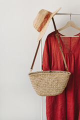 Elegant fashion clothes and accessories. Red dress, straw hat, straw handbag on hanger. Fashion...