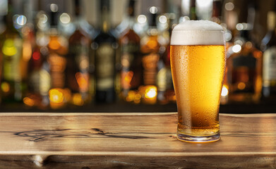 Glass of chilled beer on wooden bar table top and blurred bar interior at the background.
