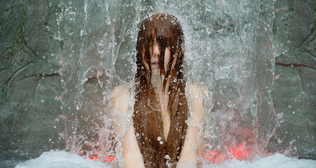 beautiful young cute sexy Portrait of a redhead woman under the splashing pattering waterfall, burbling water in the spa wellness pool, hair in her face