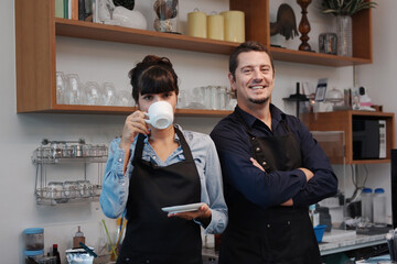 Smiling Caucasian Young barista couple love or partnership is wearing apron and drinking coffee relax in the coffee shop. Start up for small cafe business owner concept