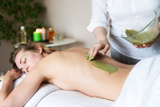 Beautiful relaxed woman having clay mask applying by beautician