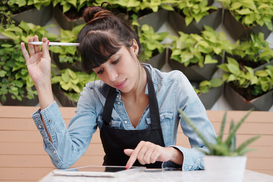 Smiling Caucasian Young barista woman is wearing apron and thinking online marketing business on tablet in cafe and coffee shop. Start up small cafe business and technology Concept