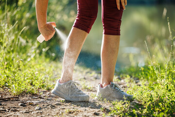 Woman spraying insect repellent against mosquito and tick on her leg before jogging in nature