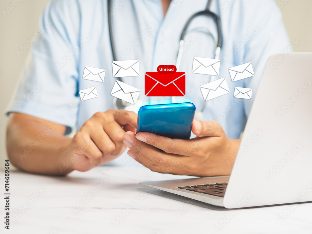 Poster doctor using a mobile receives a new message with unread email icons while sitting at a desk.