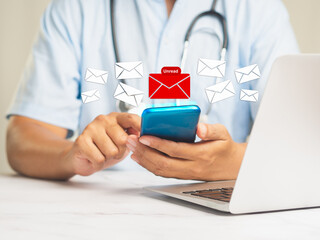 Doctor using a mobile receives a new message with unread email icons while sitting at a desk.