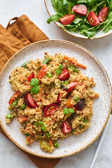 Vegan warm salad made with couscous, tomatoes, green beans, mint, roasted carrots and sweet peppers. Couscous with vegetables in bowl on light background. Variation of Tabbouleh Salad.