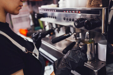 Barista in black gloves presses the button for pouring boiling water into metal cup
