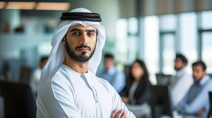 Serious arab at office wearing kandura looking at front ideal for Middle East business concept. Arabic man inside a corporate establishment with colleagues at the background. 