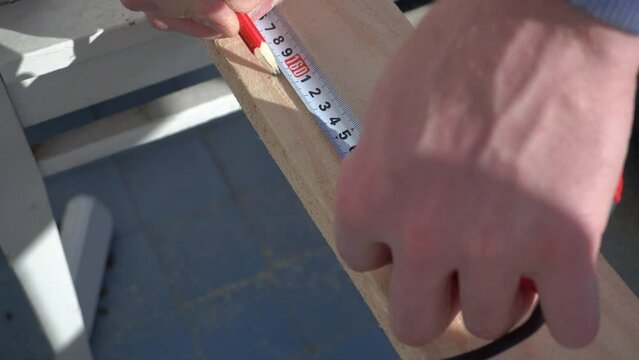 Close-up of male hands measuring with tape measure. Male hands making a mark on a wooden board.