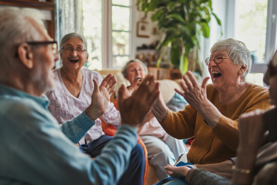 Happy Seniors Clapping And Celebrating Together, Showcasing Group Enjoyment And Lively Spirit In A Home Setting