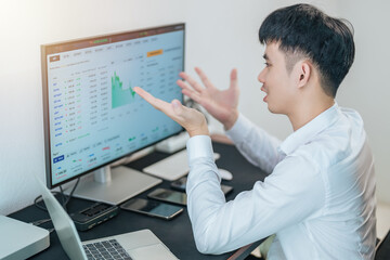 Handsome young businessman is trading the stock market via computer and smartphone.