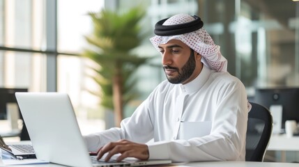 Successful Arab Businessman in White Traditional Outfit Sitting in Office and Working on Laptop Computer. Business Manager Planning Corporate Strategy. Saudi, Emirati, Arab Businessman Concept. 