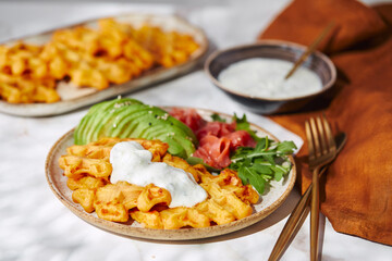 Hearty sweet potato or pumpkin waffles with avocado, salmon, arugula and sauce