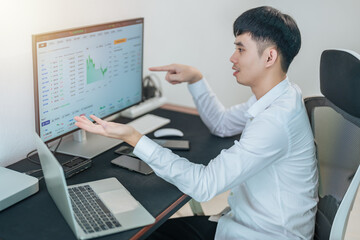 Handsome young businessman is trading the stock market via computer and smartphone.