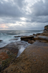 Cloudy sunrise view over a rocky coastline.