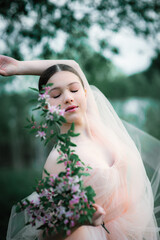 Portrait of a young young dancer in an airy long beige dress and a veil on her head with a bouquet of wildflowers among spring nature.