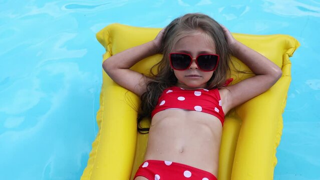 Cute little girl lying on inflatable mattress in swimming pool with blue water on warm summer day on tropical vacations. Summertime activities concept. Cute little girl sunbathing on air mattress