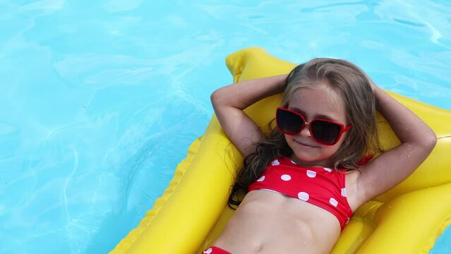 Cute little girl lying on inflatable mattress in swimming pool with blue water on warm summer day on tropical vacations. Summertime activities concept. Cute little girl sunbathing on air mattress