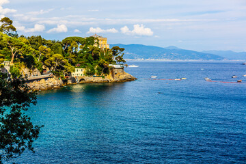Fototapeta premium Fishing boats moored on water in harbor of Ligurian and Mediterranean Sea near coastline of Riviera di Levante of National park Cinque Terre Coast with blue sky, Riomaggiore village, Liguria, Italy.