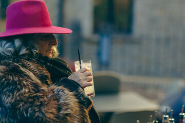 senior east european classy woman drink sip a tom collins cocktail outdoors in winter time at event