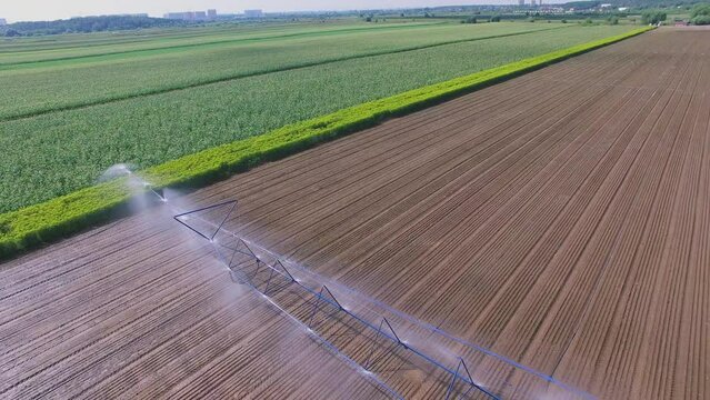 Tractor moves watering system across farm field at summer