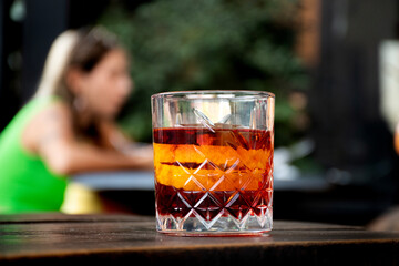 glass of red negroni cocktail with orange slices and clear ice block on wooden table background...