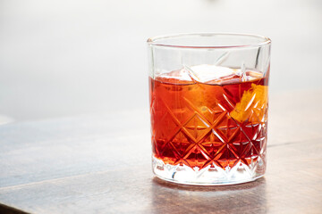 glass of red negroni cocktail with orange slices and clear ice block on wooden table bright background