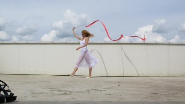 Dancer with a red ribbon posing on the roof for a photographer