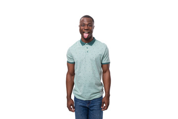 Fototapeta premium young handsome african guy with short haircut dressed in a mint t-shirt and jeans shows his tongue