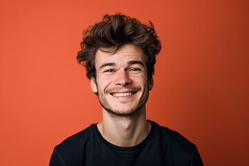 A man with a beard is smiling in front of an orange background