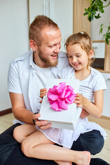 Smiling Father and Daughter Sharing a Gift Box With a Pink Bow Indoors
