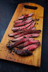 Traditional barbecue wagyu gourmet flank steak sliced with black salt and chili served as close-up on a wooden design cutting board