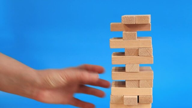 A woman plays Jenga on a blue bright background. The concept of family vacation, holidays, entertainment. A woman's hand takes out a block from a wooden toy tower. Game