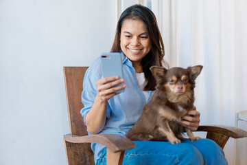 Young woman have a break at work for making selfie with her domestic pet. Young Woman Using Smartphone With Her Dog At Home.