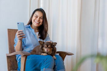 Young woman have a break at work for making selfie with her domestic pet. Young Woman Using Smartphone With Her Dog At Home.